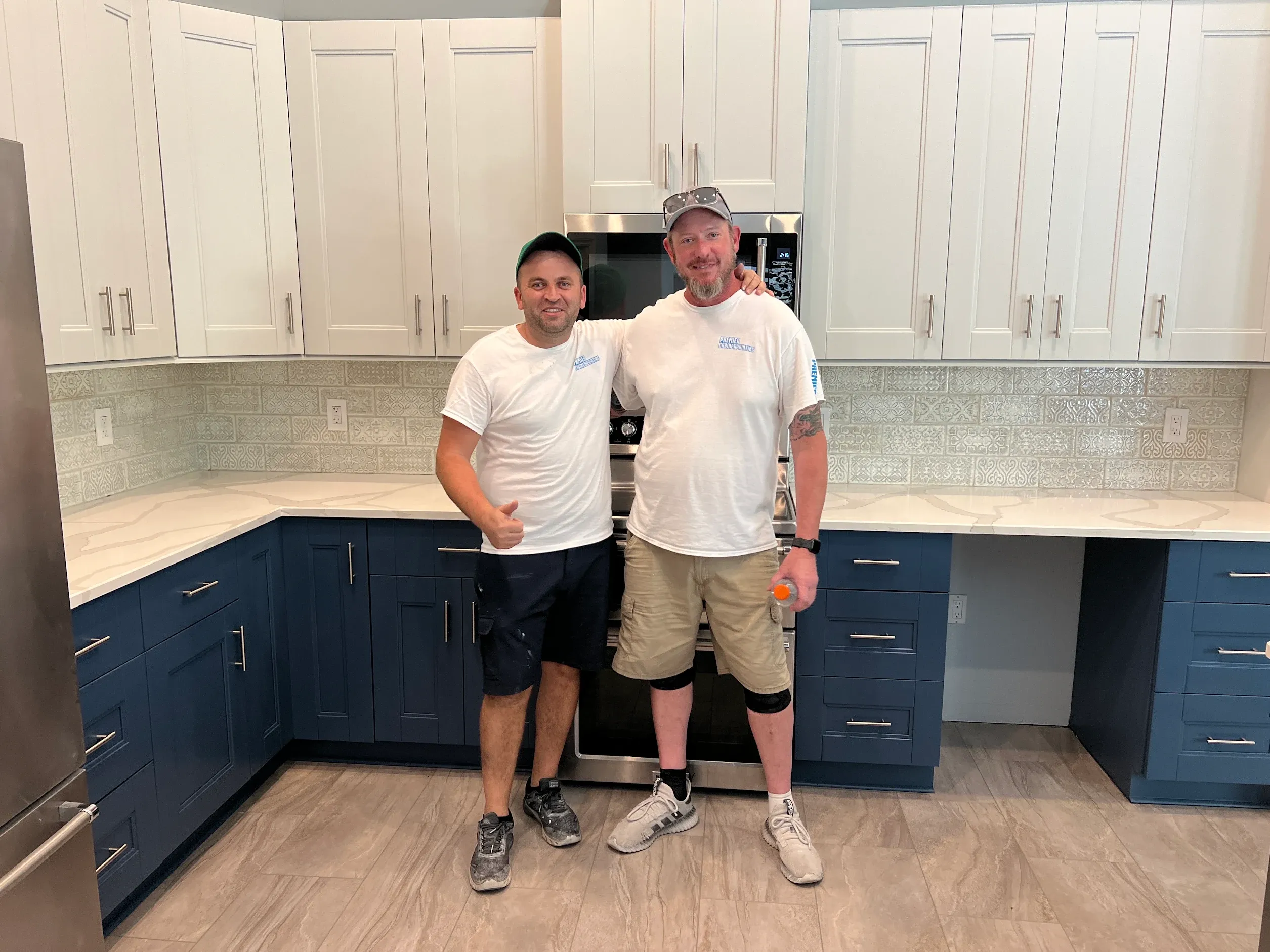 Two Premier technicians standing in a Palm Harbor kitchen they finished, with Arctic Gray upper cabinets and Van Deusen Blue lower cabinets